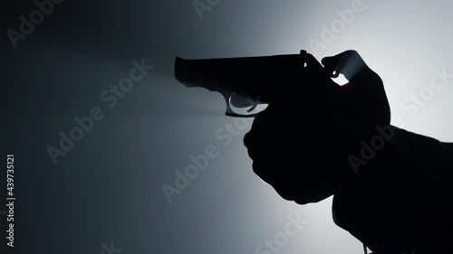 Silhouette male hand cocking gun trigger. Unknown criminal cocking trigger.