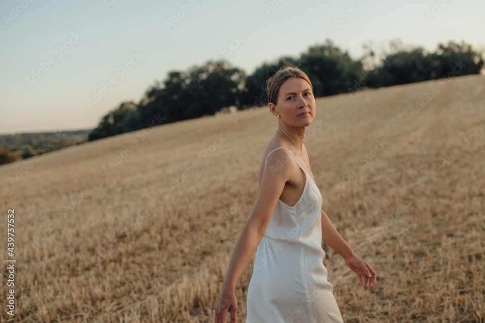 Woman in white looking back while walking on a field Woman in white looking back while walking on a field