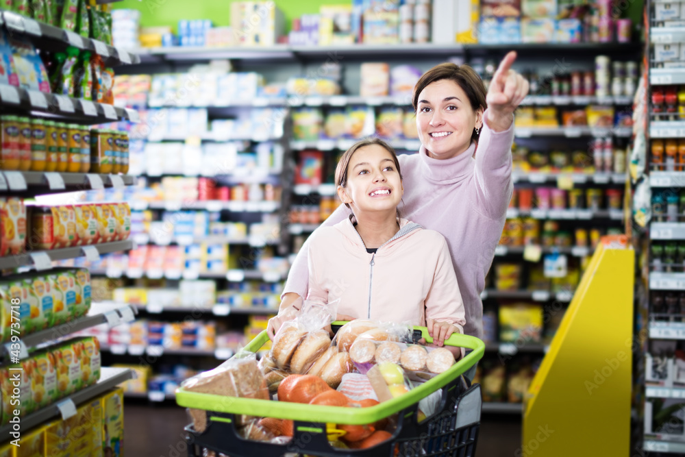 Attractive female customer with teenage daughter restocking for family in supermarket