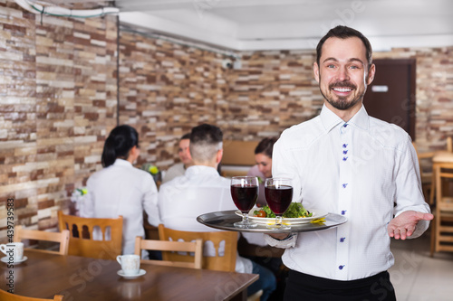 Cheerful male waiter serving a rural restaurant guests at table