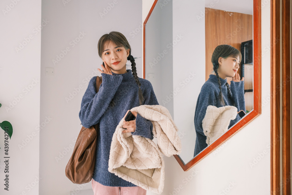 © Pansfun Images/Stocksy - Young Asian female holding mobile phone and coat in front of the