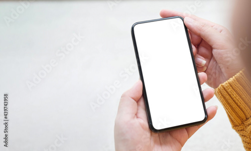 Mockup image blank white screen cell phone.women hand holding texting using mobile on desk at home office. © wichayada