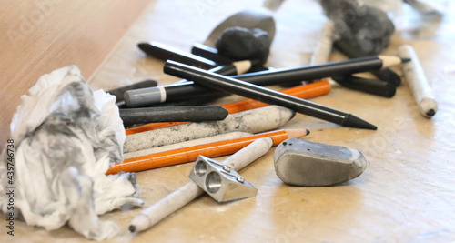 Close up detail of a variety of drawing media an artist or drawer would use creatively. Charcoal, pencils, sharpener and other artistic products on a table being used. Art equipment on a table.