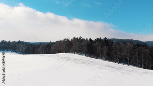 Panoramic view of the snow-covered sloppy landscape in Ojcowski Park Narodowy Krakow, Poland. Ever green trees in the background against cloudy blue sky. Bright sunny day in winter season. 