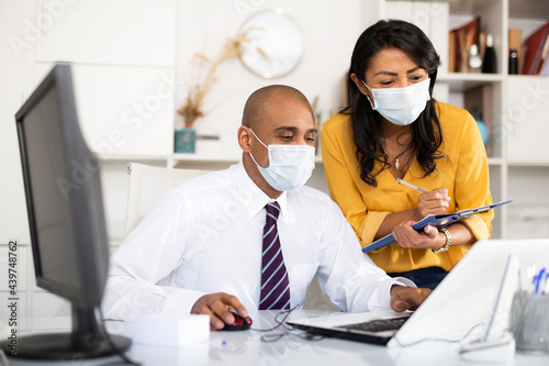 Manager in protective medical mask gives task to assistant at office