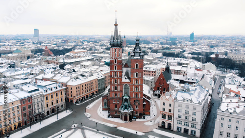 Aerial view of the Krakow   s Rynek G  owny  Central Square  surrounded by historic buildings. Twin towers of the Basilica of Saint Mary against clear white sky in the background. City Skyline.