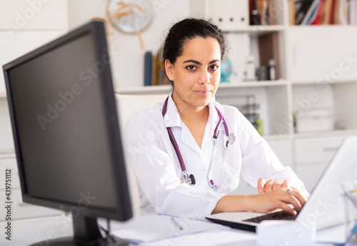 Portrait of female doctor who is working with laptop and documents