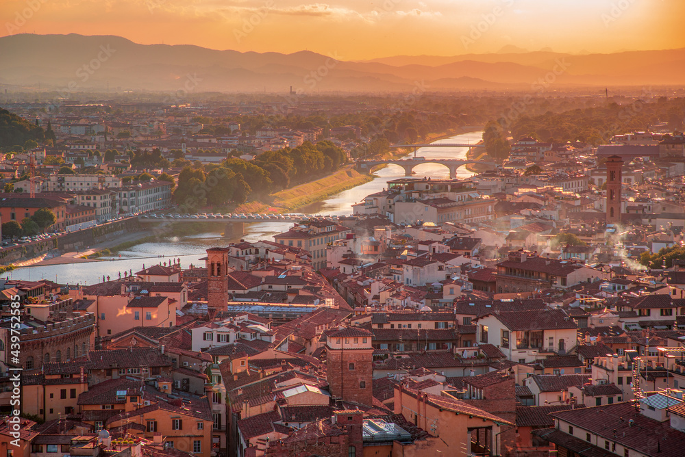 Florence, Italy - 20 June, 2019 :  panoramic overview from Arnolfo Tower (Torre di Arnolfo)at sunset haze, historical part of the city, River Arno and mountains range in sunset rays on the background 