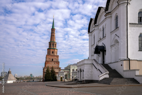 The leaning Suyumbike Tower in the Kazan Kremlin and the main entrance to the Annunciation Cathedral in the foreground on a sunny, cloudy spring morning, Kazan, Tatarstan, Russia.