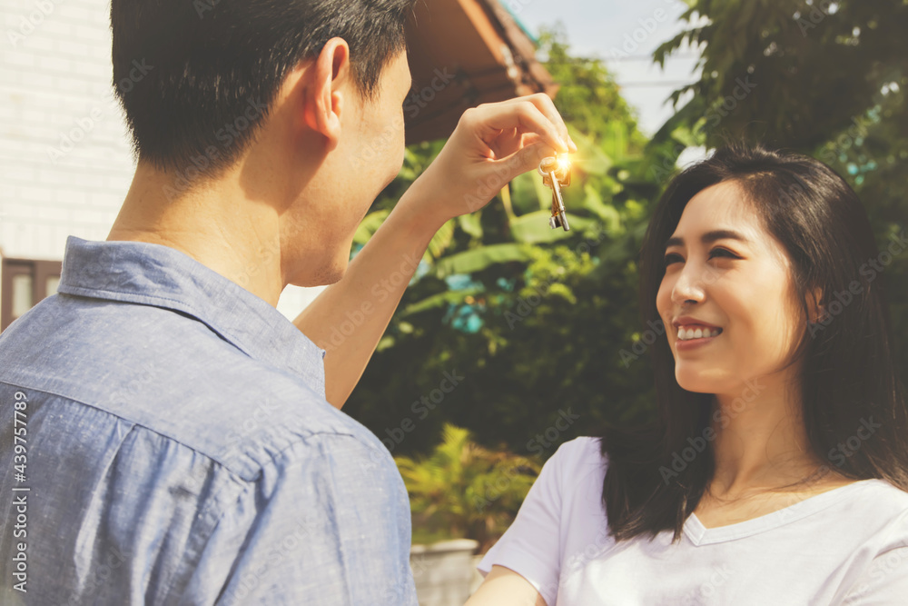 Obraz premium Family planning with a new home : Surprise asian couple husband presents house keys to beautiful wife showing ownership with pride : Portrait happy young woman looking at the keys to a new house