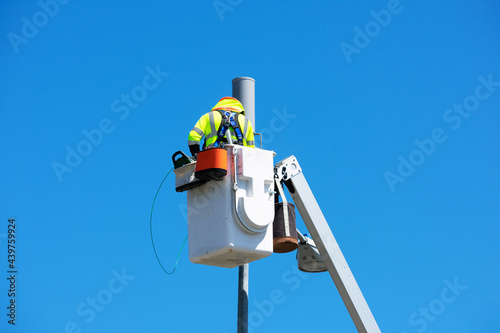 Technician works on installing or repairing a small cell antenna on a lamp post from the platform of the telescopic boom lift. Blue sky photo