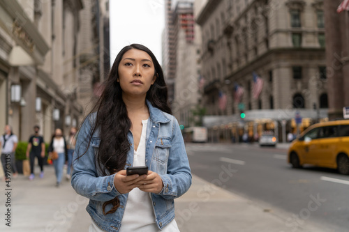 Young Asian woman in city walking texting cellphone on a street © blvdone