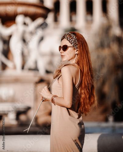 Fotografija Portrait of young wealthy redhead woman in sunglasses and summer dress standing