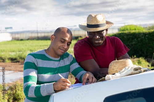 Portrait of african and hispanic male gardeners signing papers outside