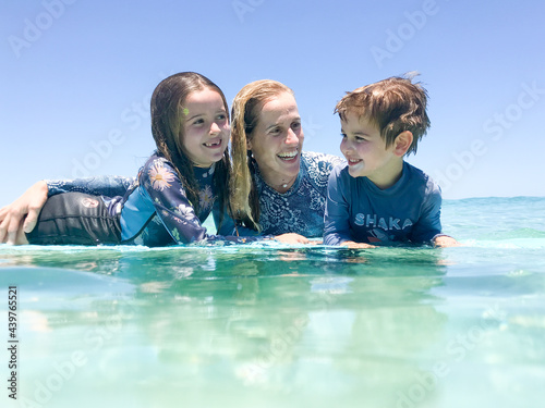Portrait of Mother and two children in ocean leaning on surfboard photo