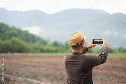 Young Asian men travel to beautiful nature. He was standing on the roadside. He uses his phone to take pictures of beautiful views.