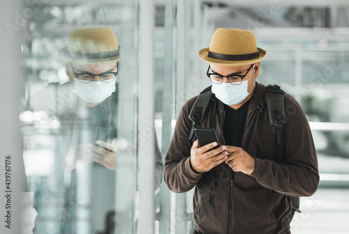 Young traveler man wearing mask to protect flu coronavirus using smartphone to check in Arrival or departure passenger. Tourist in airport terminal. Backpacker travel in downtown urban city