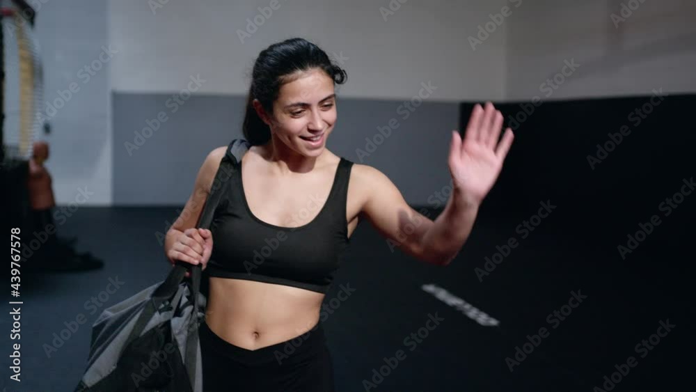 Woman with ponytail in black clothes walks carrying sports bag along the gym dressing to say goodbye to her coach. Woman with ponytail in black clothes walks carrying sports bag along the gym dressing to say goodbye to her coach.