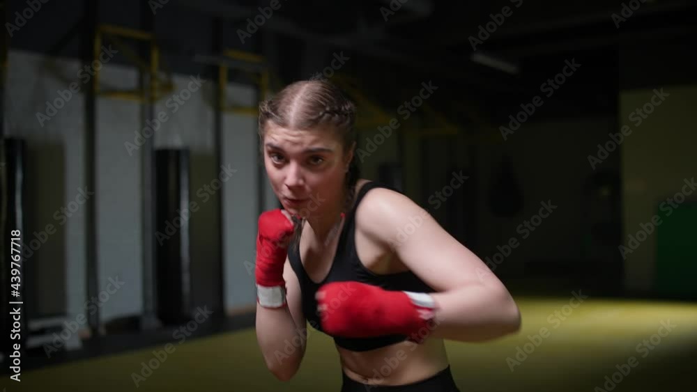 Woman fighter trains his punches, training in the boxing gym, young woman looks at the camera and trains a series of punches, front view. Woman fighter trains his punches, training in the boxing gym, young woman looks at the camera and trains a series of punches, front view.
