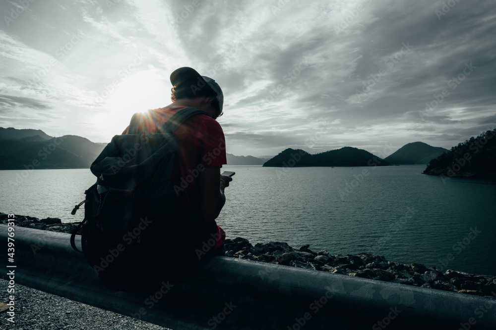 Fototapeta premium young teen Caucasian boy hipster man adult backpacker enjoying camera on beautiful landscape scenery view jungle mountains forest at Kanchanaburi water river dam National Park, Thailand.