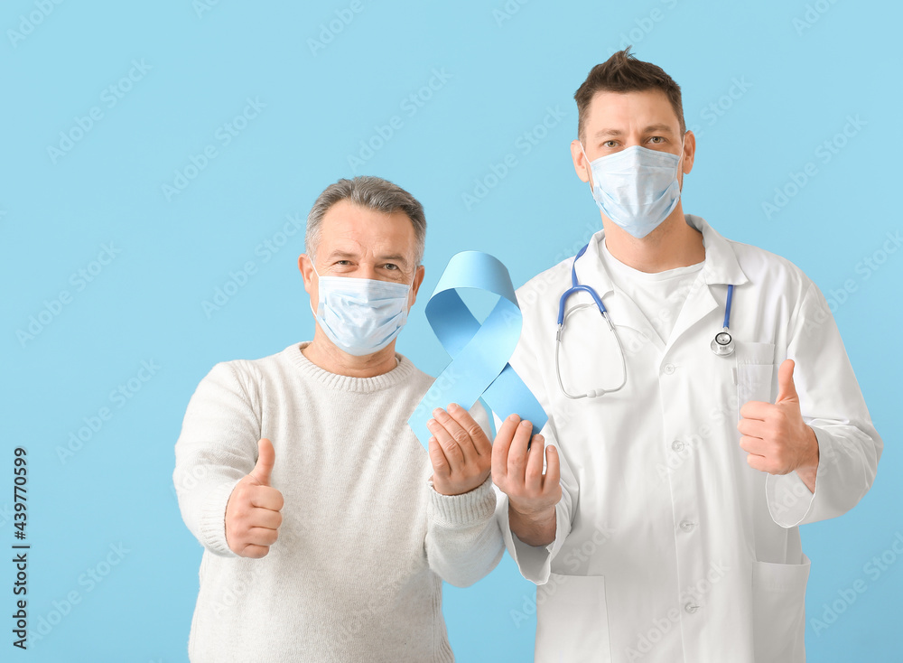 Doctor and mature man with blue ribbon showing thumb-up gesture on color background. Prostate cancer awareness concept