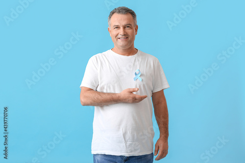 Mature man with blue ribbon on color background. Prostate cancer awareness concept photo