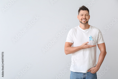 Man with blue ribbon on light background. Prostate cancer awareness concept photo