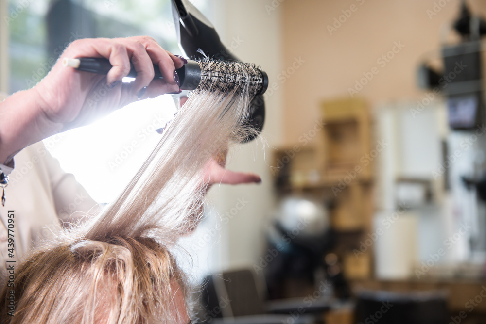Fototapeta premium hairdresser working with the brush and dryer on a client, with blonde hair in the hair salon. beauty salon