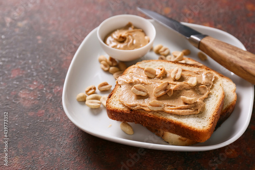 Plate with tasty peanut butter and bread on color background