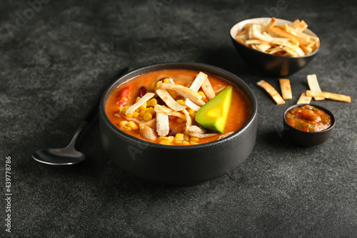 Bowl of tasty chicken enchilada soup on dark background
