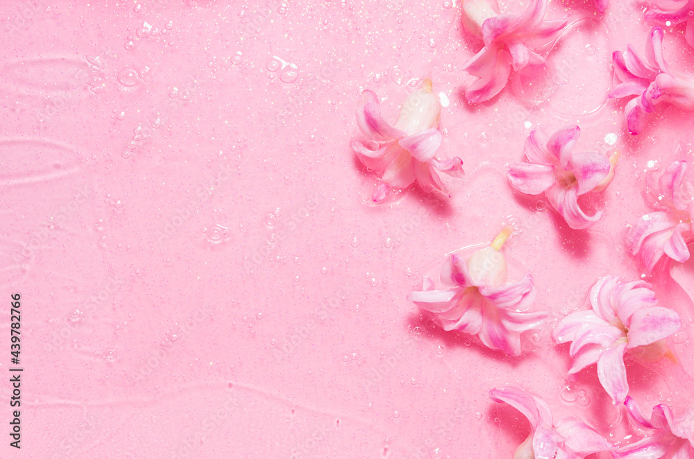 Fototapeta premium Spring gentle girlish floral cosmetic background - pink hyacinth flowers with transparent moisturizing gel with gold shimmer glitter, top view, copy space, border.