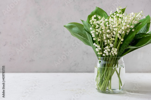 Vase with beautiful lily-of-the-valley flowers on light background