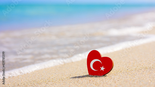 Fototapeta Naklejka Na Ścianę i Meble -  Turkish flag in the shape of a heart on a sandy beach. The concept of the best vacation in Turkey