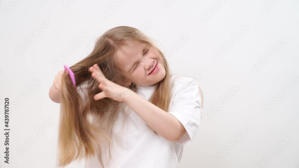 fun little girl combs long and tangled hair on a white background. cosmetics for the care of children's hair. fun little girl combs long and tangled hair on a white background. cosmetics for the care of children's hair.