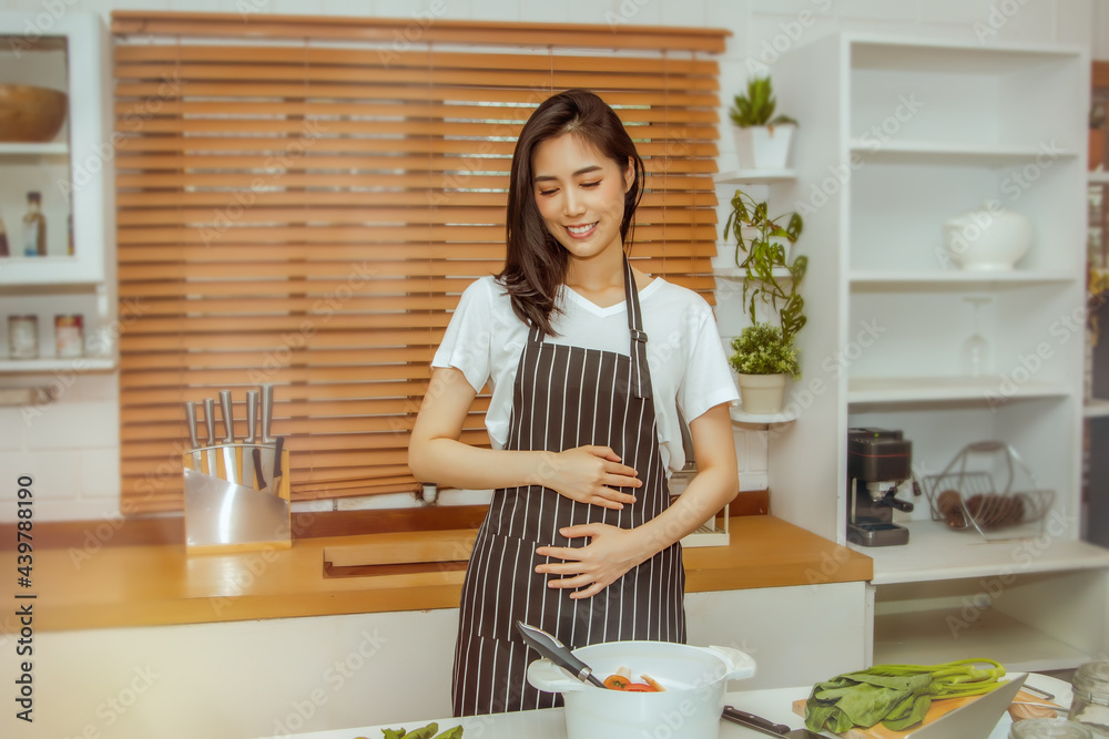 Concept of caring for the fetus : Beautiful Asian woman is pregnant, using her hands to touch the womb with love and choosing to cook fresh vegetables, nutritious food for her and her fetus. Concept of caring for the fetus : Beautiful Asian woman is pregnant, using her hands to touch the womb with love and choosing to cook fresh vegetables, nutritious food for her and her fetus.