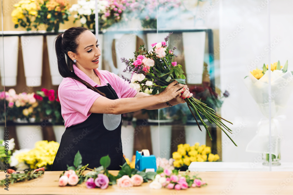 An attractive young female florist works in a flower shop and makes flower arrangements for sale