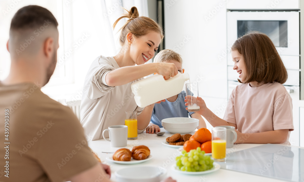 Young happy family with two cute little kids having breakfast together in kitchen and smiling Young happy family with two cute little kids having breakfast together in kitchen and smiling