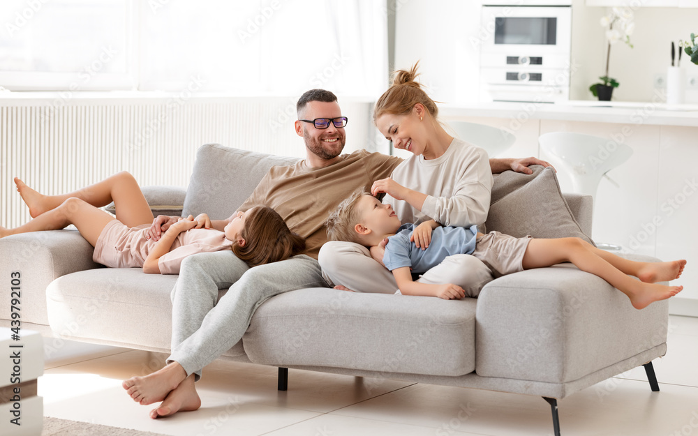 Young loving parents with two kids relaxing on sofa at home, enjoying leisure time together