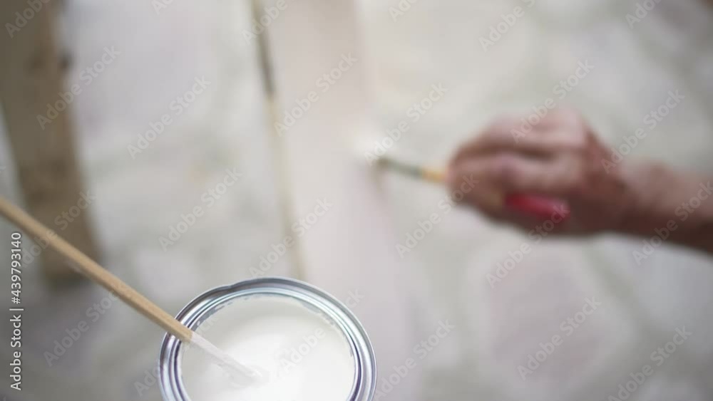 Closeup on a renovator carpenter's hand painting in white an old wooden table in Shabby Chic style. Focus on the can of paint. Closeup on a renovator carpenter's hand painting in white an old wooden table in Shabby Chic style. Focus on the can of paint.
