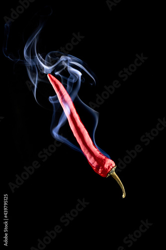 Chilli peppers isolated. Spicy chile cayenne pepper with abstract fog or steam mist cloud. Red hot chili paprika with tongue of fire flame on black background. Fresh spice vegetable concept.