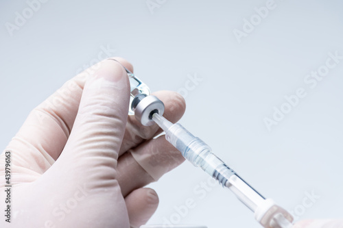 Doctor hand wears white medical glove holding flu, covid-19 liquid vaccine vial bottle and syringe are filling for preparing injection. Vaccination for fight Covid-19 virus concept.
