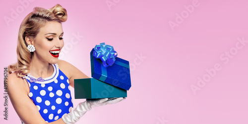 Image of beautiful young happy woman dressed in pin up style blue dress in polka dot and white gloves, on pink background. Caucasian blond model posing in retro fashion studio concept. Wide. photo