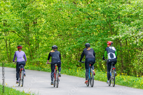 Women who exercise on bicycles on a road in a deciduous forest