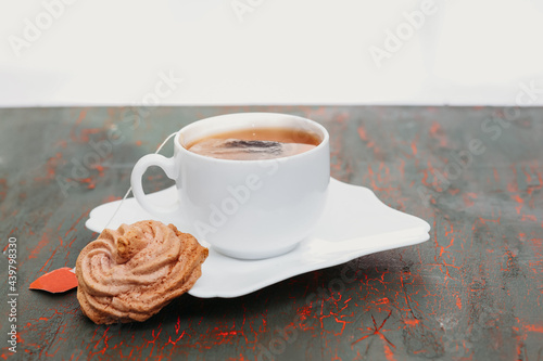 White cup of fragrant tea on a black and red background and a slice of macaroons, a tea bag with an empty red label.