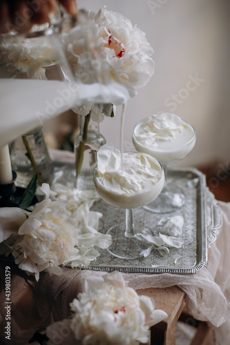 milk flows beautifully over a transparent glass. pour milk into a glass with white petals. white peonies flowers and petals.