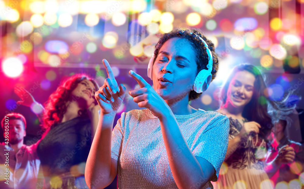 nightlife, technology and people concept - happy young african american woman in headphones listening to music and dancing in neon lights over nightclub background nightlife, technology and people concept - happy young african american woman in headphones listening to music and dancing in neon lights over nightclub background