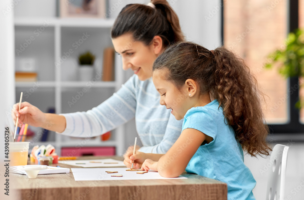 family, hobby and leisure concept - happy smiling mother spending time with her little daughter drawing or painting wooden chipboard cutouts with colors at home family, hobby and leisure concept - happy smiling mother spending time with her little daughter drawing or painting wooden chipboard cutouts with colors at home