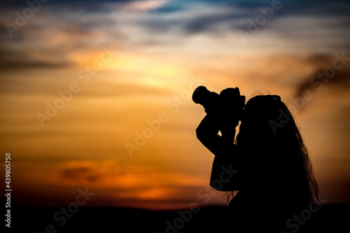 Female unrecognizable photographer silhouette, the golden hour, amazing blurred sky in the background