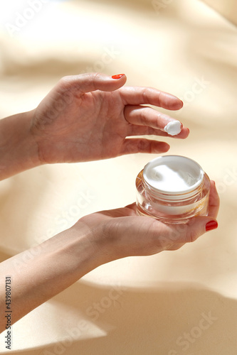 beauty product, cosmetics and people concept - female hand holding jar of moisturizer on beige background photo