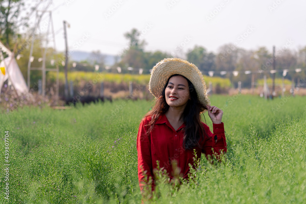 Obraz premium attractive Asian woman in red shirt with farmer hat in green leaf plant garden looking forward with happy smile face, happy young farmer in fresh green garden